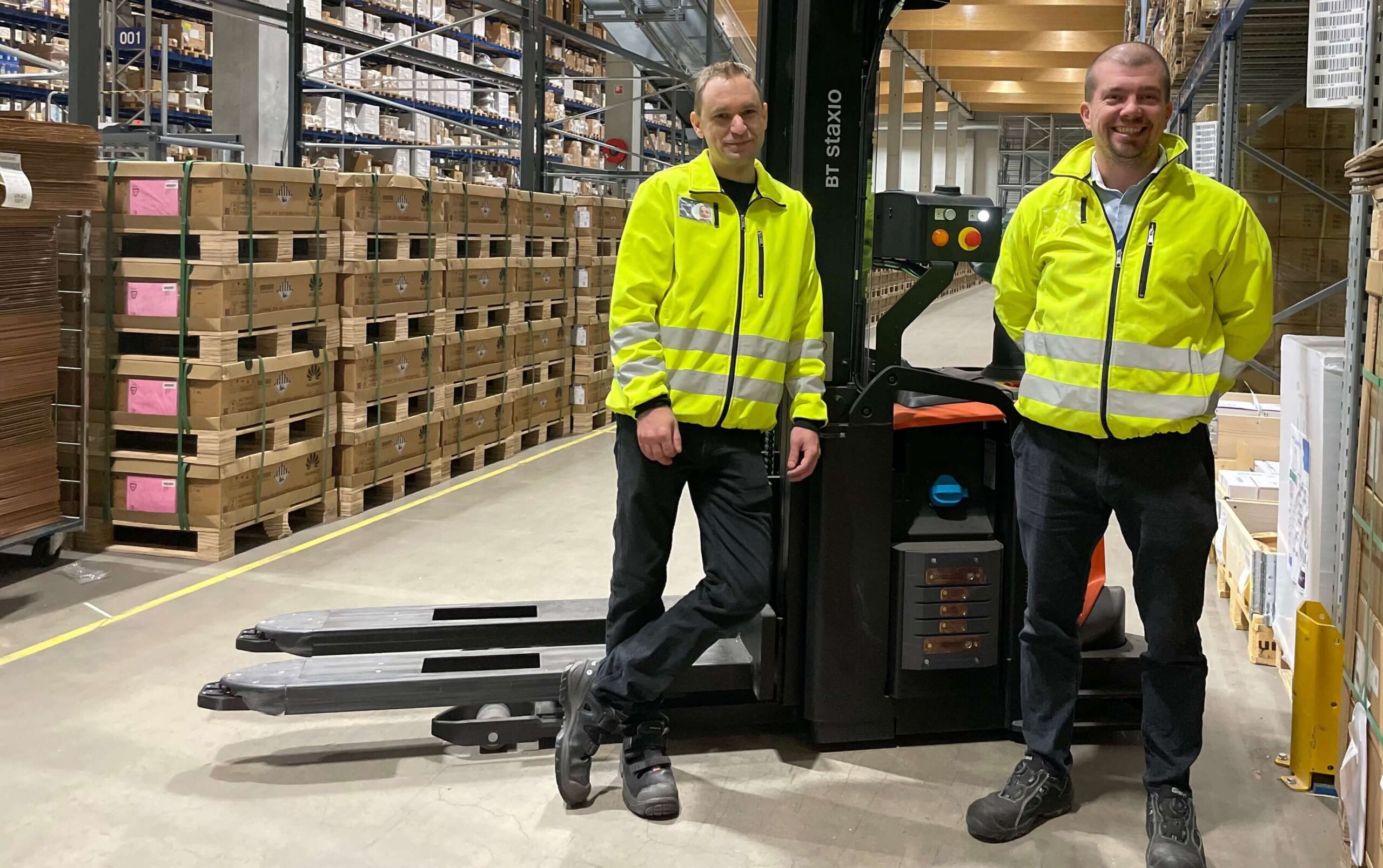 AGV lisää tehokkuutta ja parantaa turvallisuutta | Työntekijät seisovat automaattitrukin edessä ja hymyilevät kameralle.